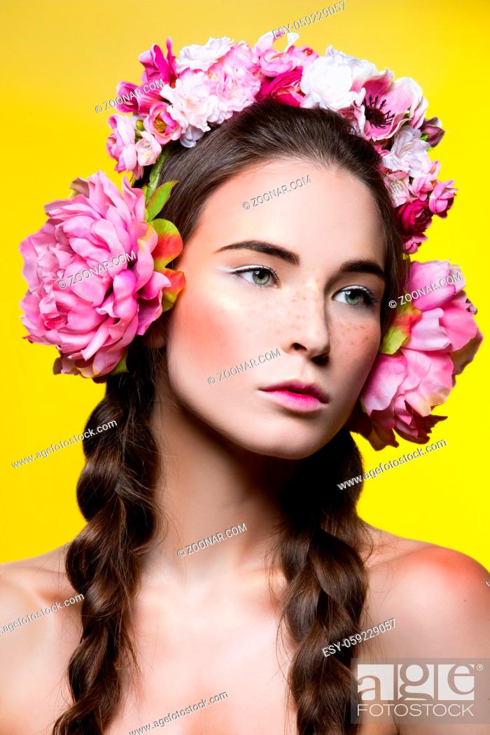 Photo de stock: Beautiful brunette young woman with braids and pink floral headphones head accessory over yellow background. Copy space.