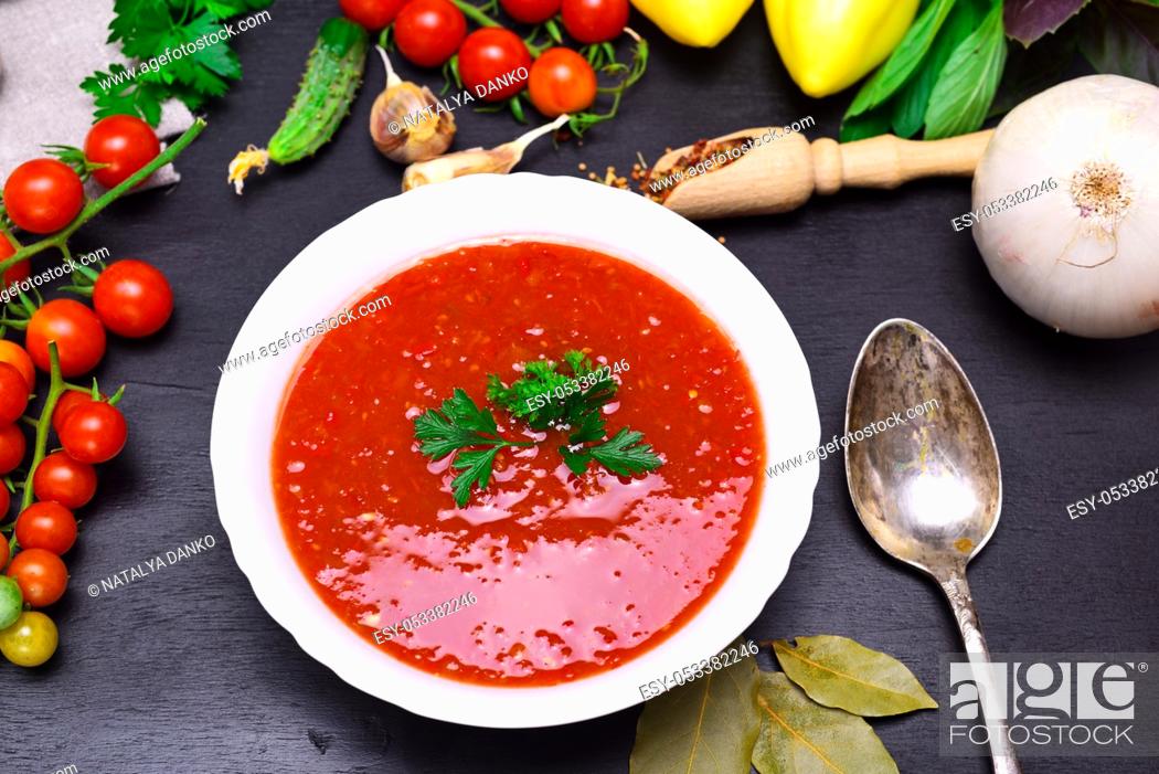 Stock Photo: Gazpacho spanish cold soup in a white round ceramic plate on a black background, next to fresh vegetables for cooking.