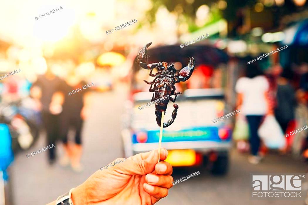 Stock Photo: Hand of the Thai vendor showing roasted scorpio. Street market in central Bangkok, Thailand.