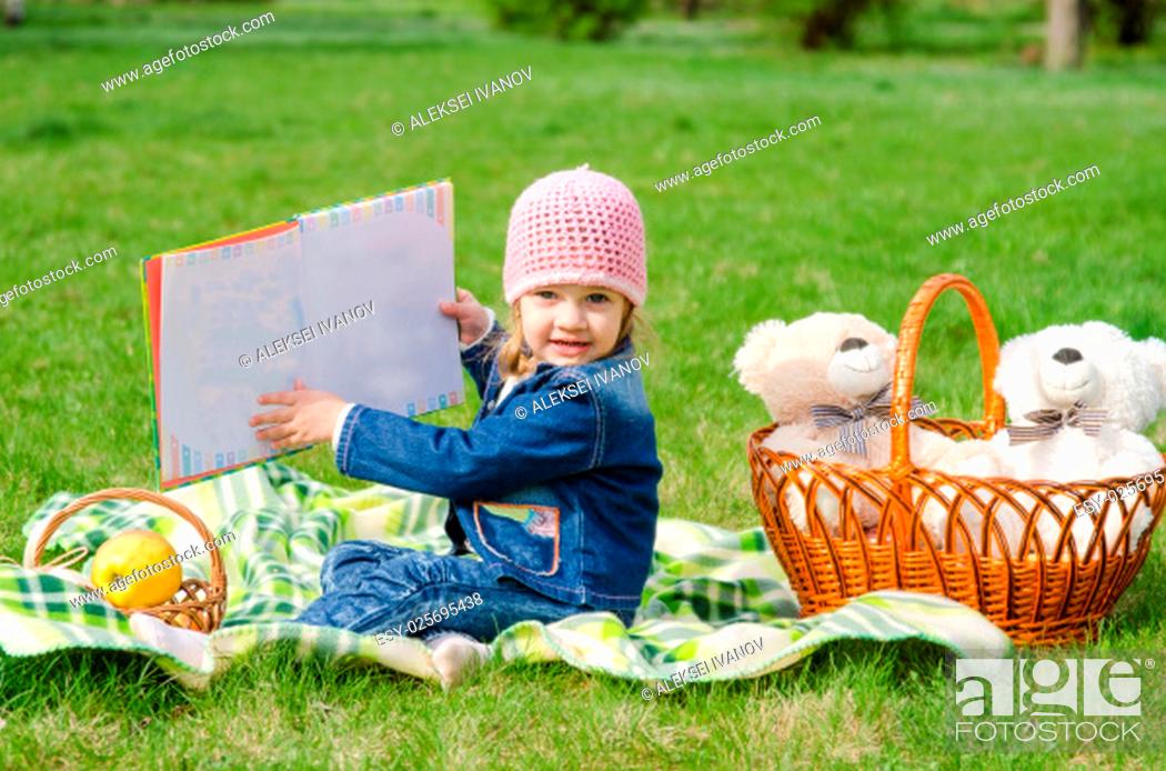 Stock Photo: The three-year girl is considering a book on picnic.