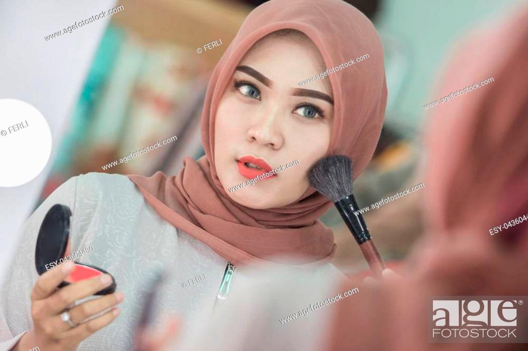 Stock Photo: Beauty muslim woman with hijab applying makeup. Beautiful girl looking in the mirror and applying cosmetic. Girl gets blush on the cheekbones.
