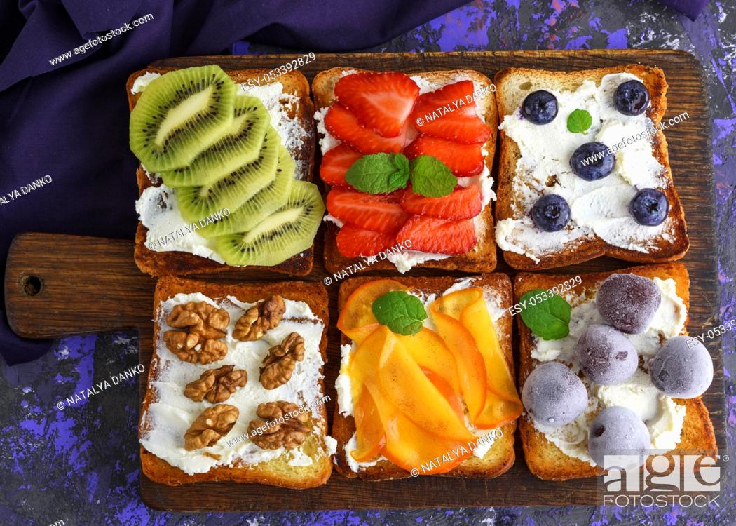Imagen: French toasts with soft cheese, strawberries, kiwi, walnuts, cherries and blueberries on a brown wooden board, top view.