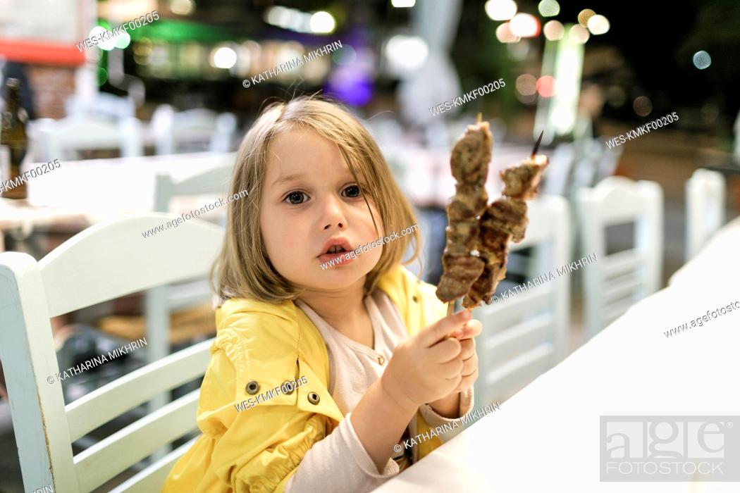 Stock Photo: Greece, portrait of little girl sitting in a restaurant with two Souvlaki meat skewers.