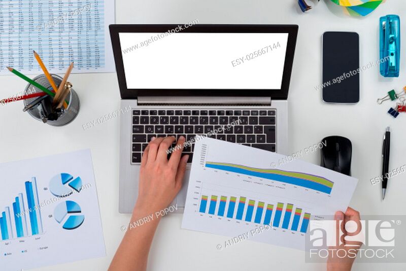 Stock Photo: High Angle View Of Person With Laptop And Graph At Desk.