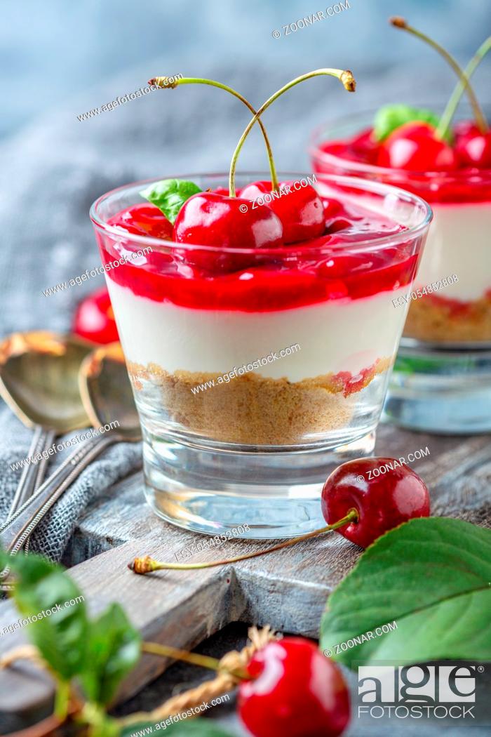 Stock Photo: Homemade cheesecake with cherry jelly in a glass close-up and fresh cherries on a wooden serving board, selective focus.