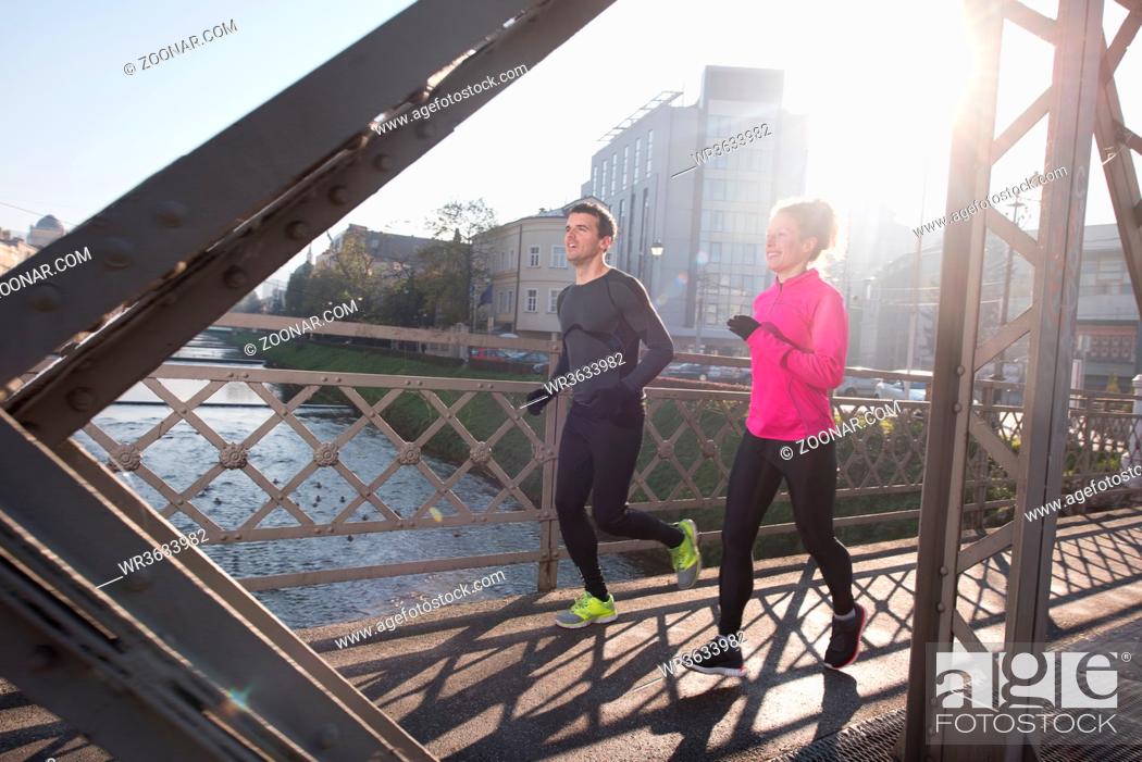 Stock Photo: healthy young couple jogging in the city at early morning with sunrise in background.