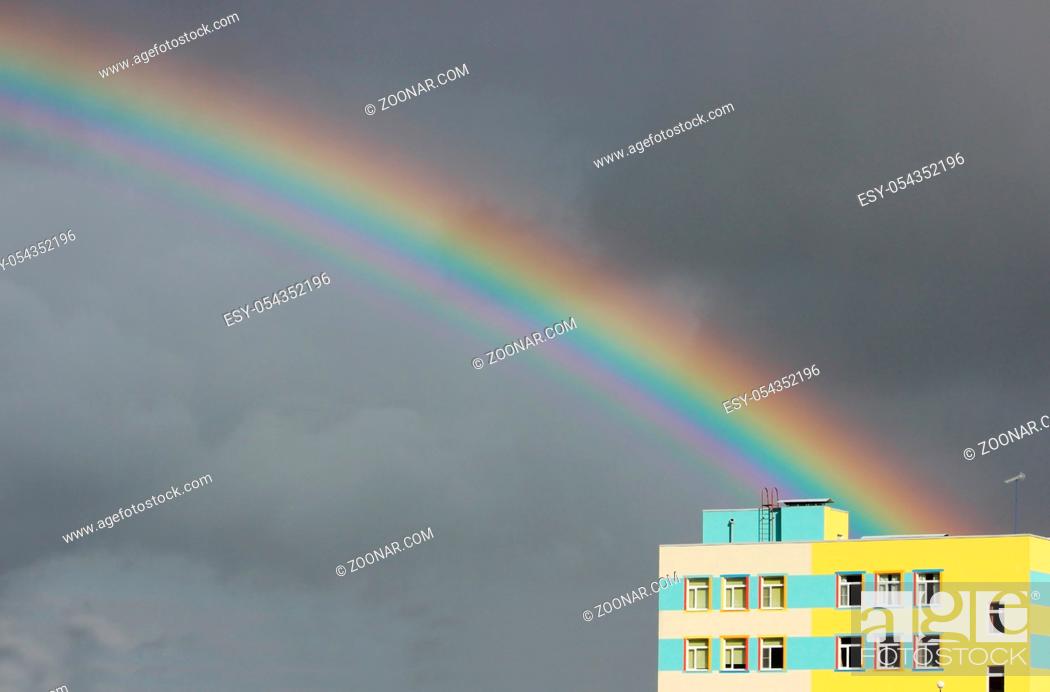 Stock Photo: Bright multi-colored wide colorful rainbow after the storm in the gray sky above the town houses.