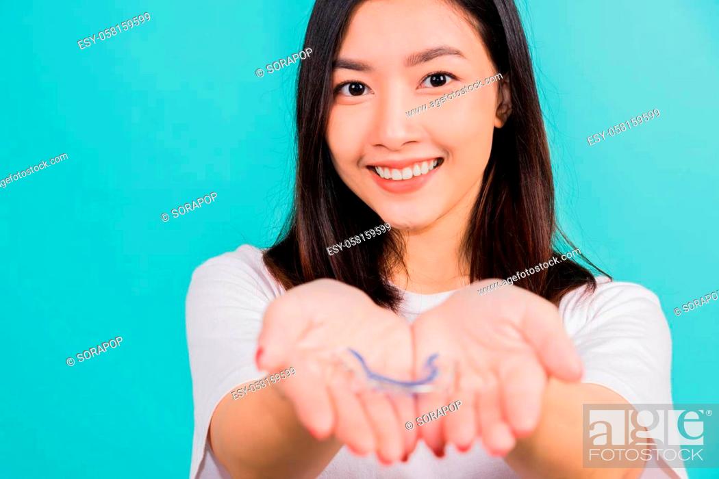 Stock Photo: Portrait young Asian beautiful woman smiling holding silicone orthodontic retainers for teeth on hand palm, Teeth retaining tools after removable braces.