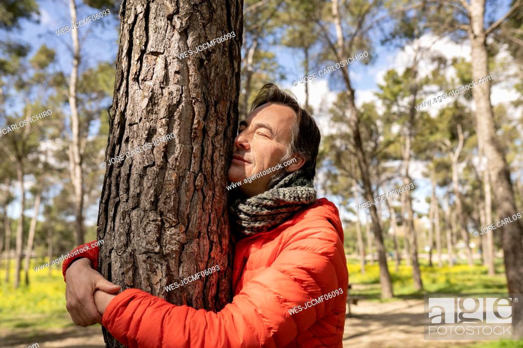 Stock Photo: Man with eyes closed hugging tree trunk in forest.
