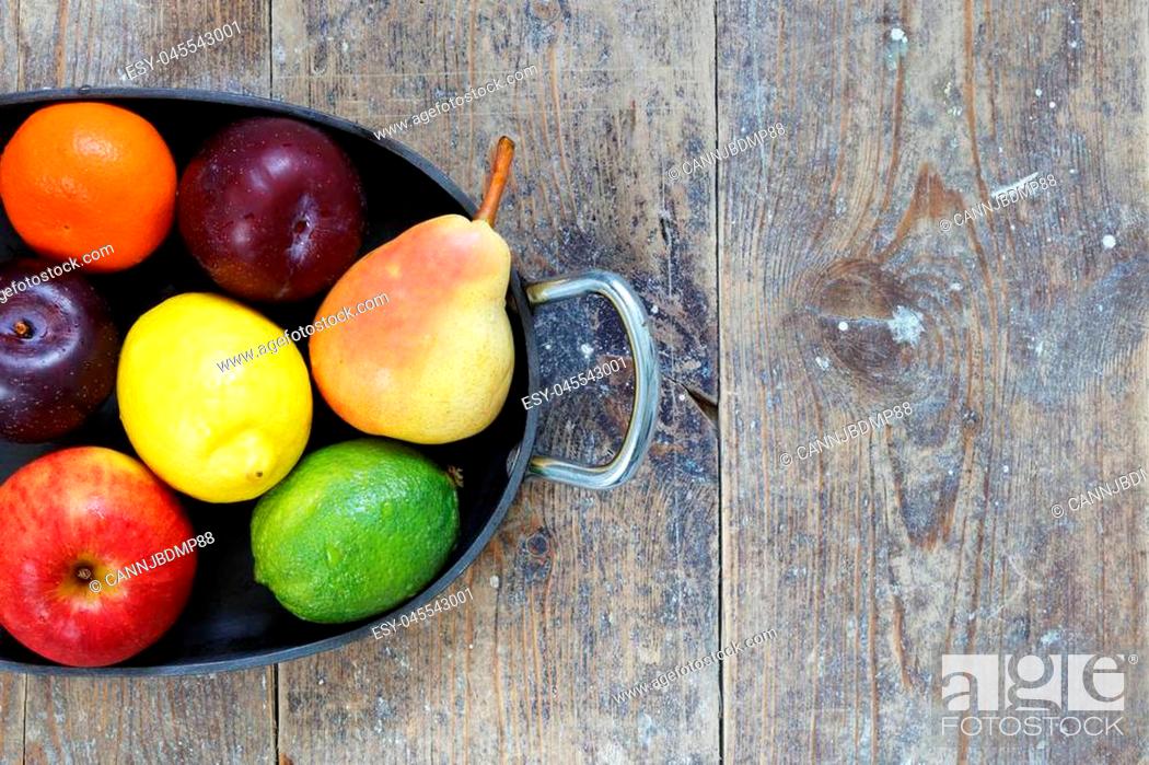 Stock Photo: Mixed fruits of apples, lime, lemon, pears and plums in metal tray on wood table with copy space right.