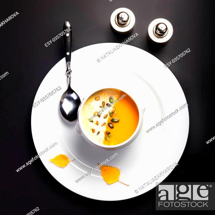Stock Photo: Pumpkin soup with cream and pumpkin seeds in a white bowl over black background.