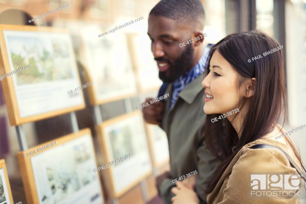 Stock Photo: Smiling young couple looking at real estate listings at storefront.