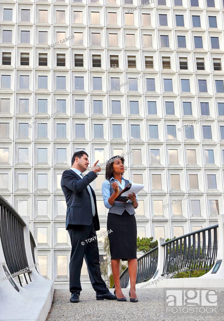 Stock Photo: Business people standing talking holding paperwork, pointing and looking upwards.