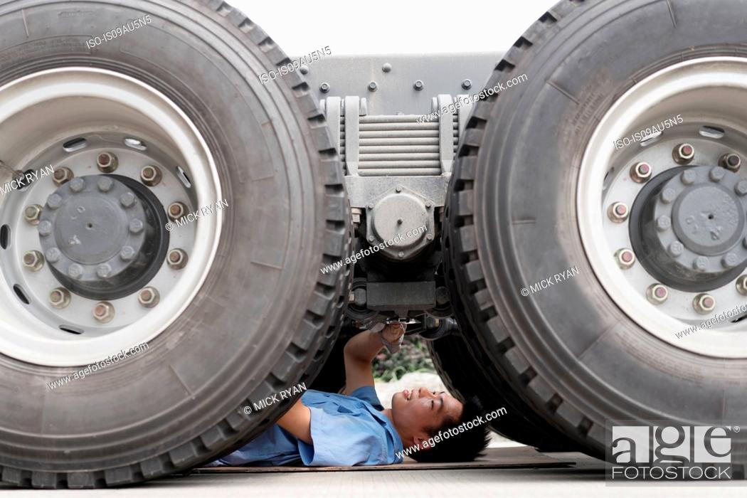 Stock Photo: Male factory worker inspecting underneath truck in crane factory, China.