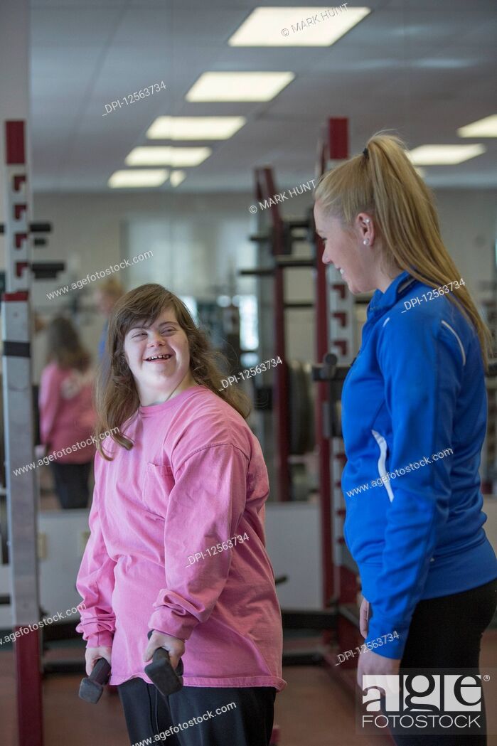 Stock Photo: Young woman with Down Syndrome working out with her trainer using weights in gym.