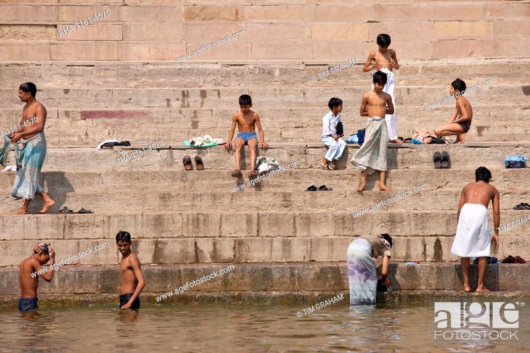 Stock Photo: Indian Hindu pilgrims men and boys bathing in The Ganges River by steps of the Ghats in Holy City of Varanasi, Benares, India.