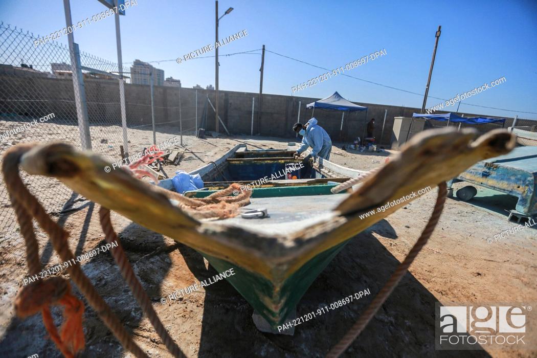 Stock Photo: 01 December 2022, Palestinian Territories, Gaza City: A Palestinian craftsman repairs a fishing boat using fibreglass at a workshop supervised by the United.