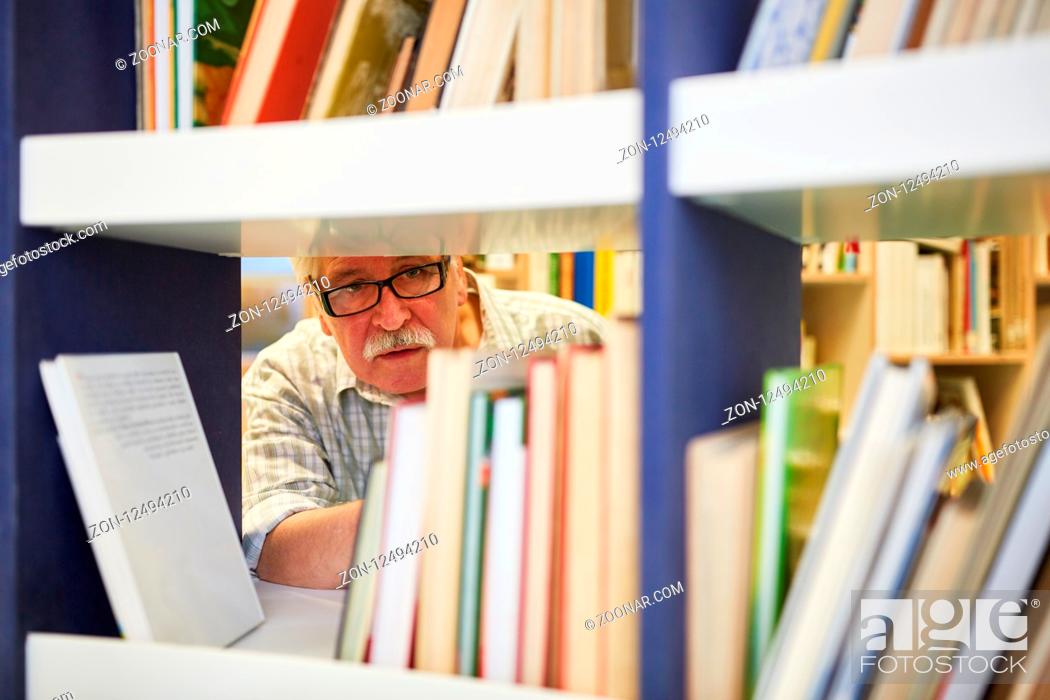 Stock Photo: Senior als Wissenschaftler recherchiert in einer Bibliothek mit vielen Büchern.