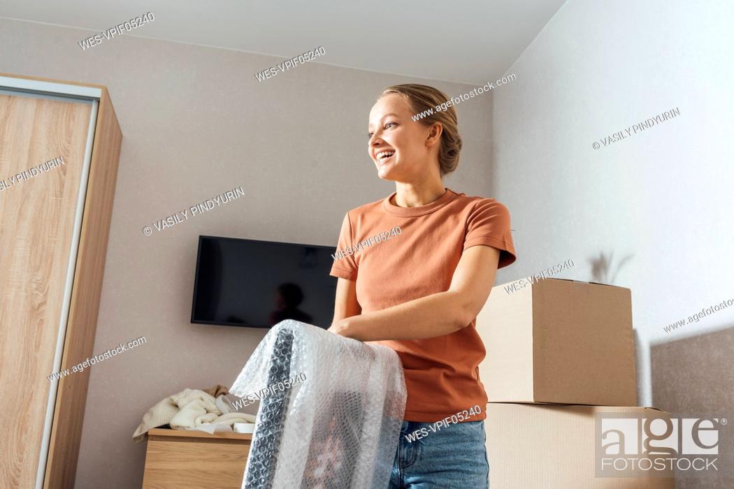 Stock Photo: Smiling woman removing bubble wrap from picture frame at home.