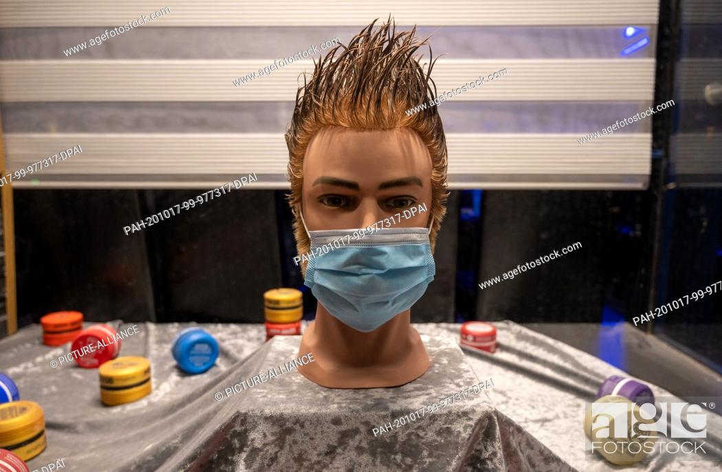 Stock Photo: 16 October 2020, Berlin: In a shop window of a hairdresser in Neukölln there is a head doll with a striking hairstyle, with a mouth-and-nose mask.