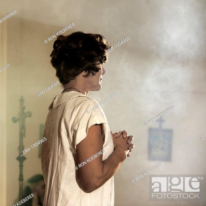 Stock Photo: A woman stands with her hands clasped in front of her chest.