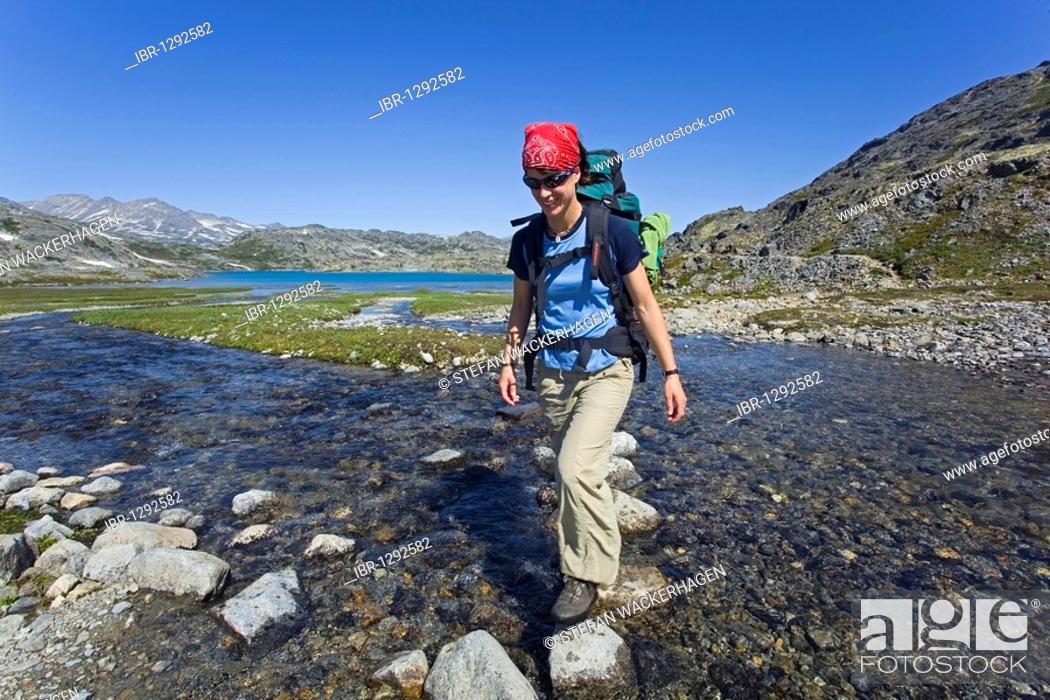 Stock Photo: Young woman, hiker with backpack, hiking, crossing creek, balancing on rocks, historic Chilkoot Pass, Chilkoot Trail, Crater Lake behind, alpine tundra.