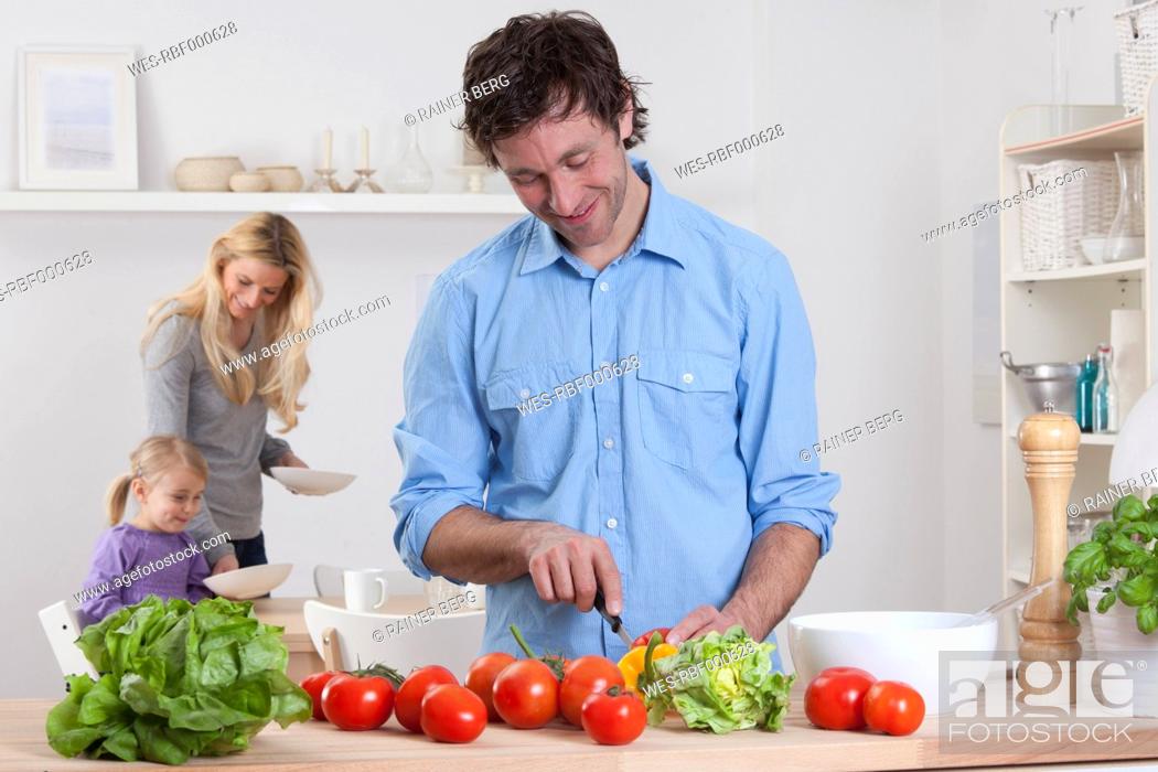 Stock Photo: Germany, Bavaria, Munich, Father preparing salad with mother and daughter in background.