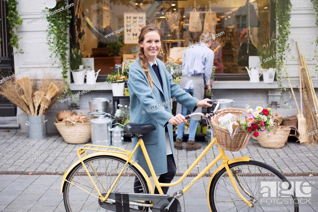 Stock Photo: Portrait smiling woman walking bicycle with flowers in basket outside storefront.