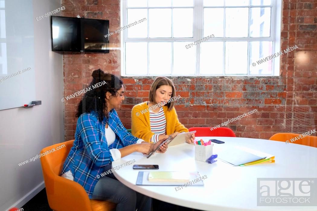 Stock Photo: Diverse female colleagues sitting at office table discussing looking at tablet.