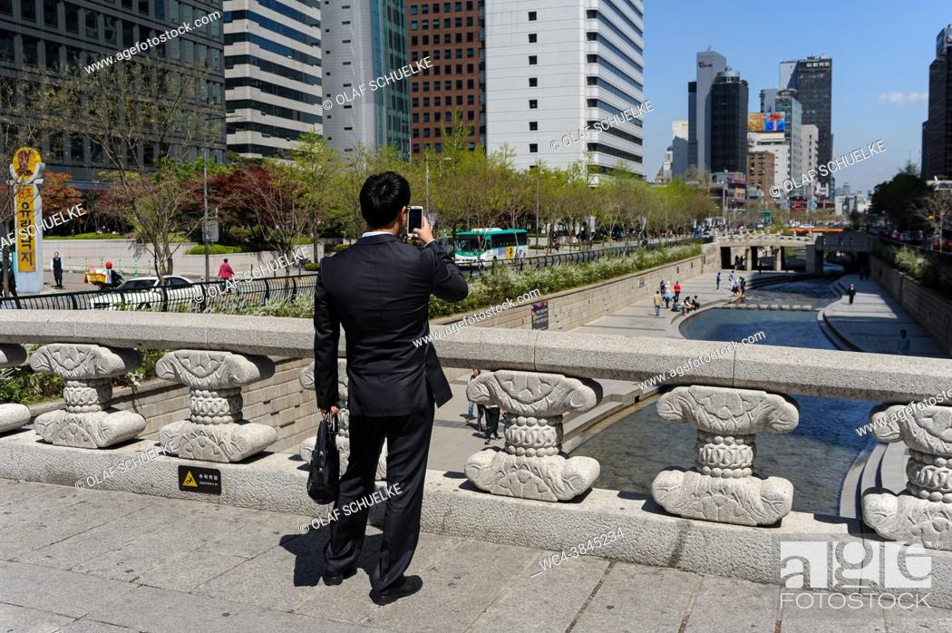 Stock Photo: Seoul, South Korea, Asia - A man takes a photo with his handphone of the Cheonggyecheon Stream and walkway in the downtown core of the South Korean capital city.