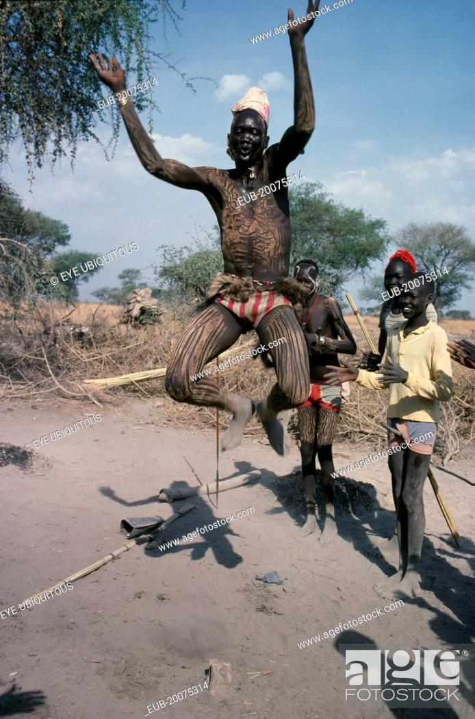 Stock Photo: Dinka tribesman with his body painted with ash leaping in to air with his arms held in the shape of the horns of a bull during dance.