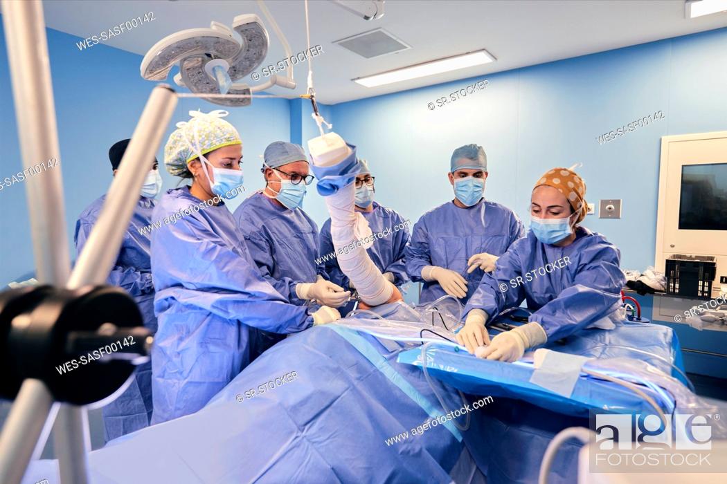 Stock Photo: Doctors wearing face mask doing arthroscopic surgery of patient while standing by table at operating room during COVID-19.