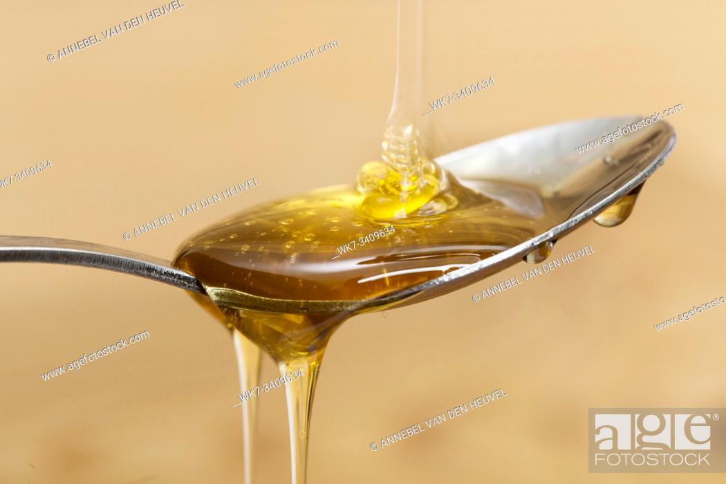 Stock Photo: Shiny golden honey dripping off of a silver spoon with a wooden brown background sweet.