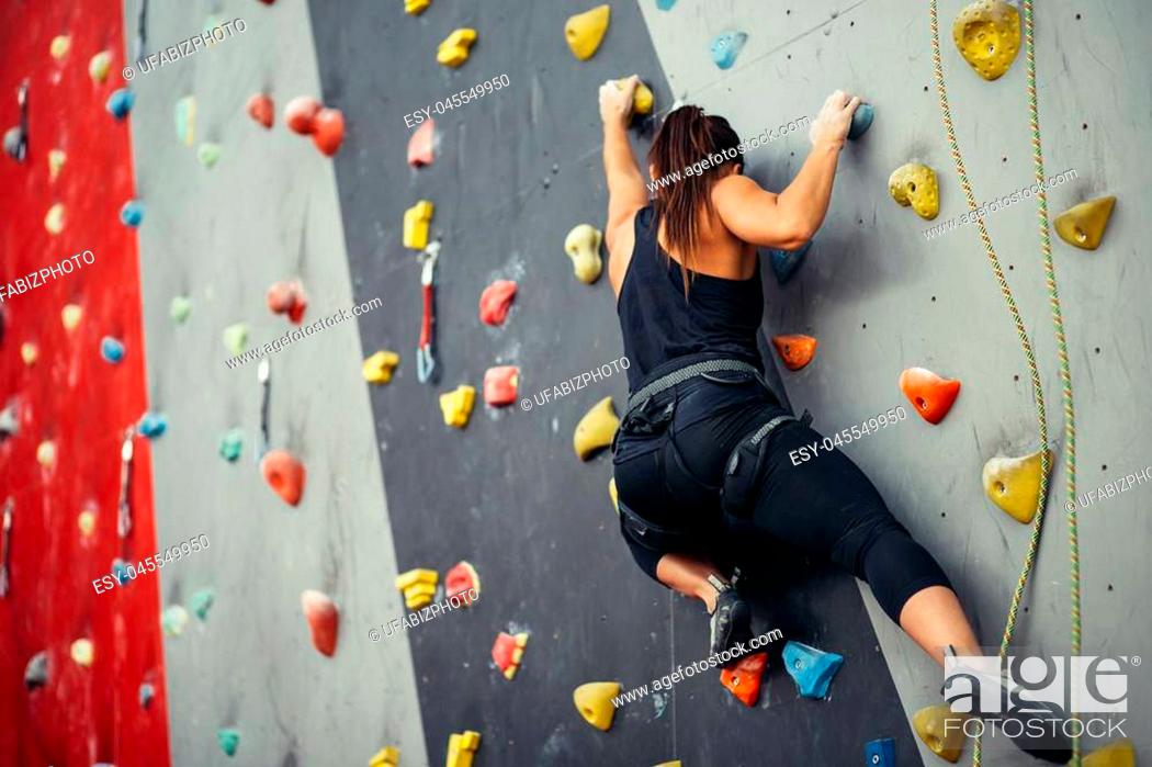 Stock Photo: Sporty young woman training in a colorful climbing gym. Free climber girl climbing up indoor.