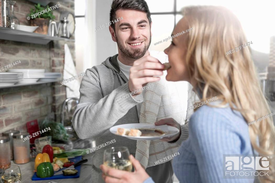 Stock Photo: Couple tasting food together in kitchen.