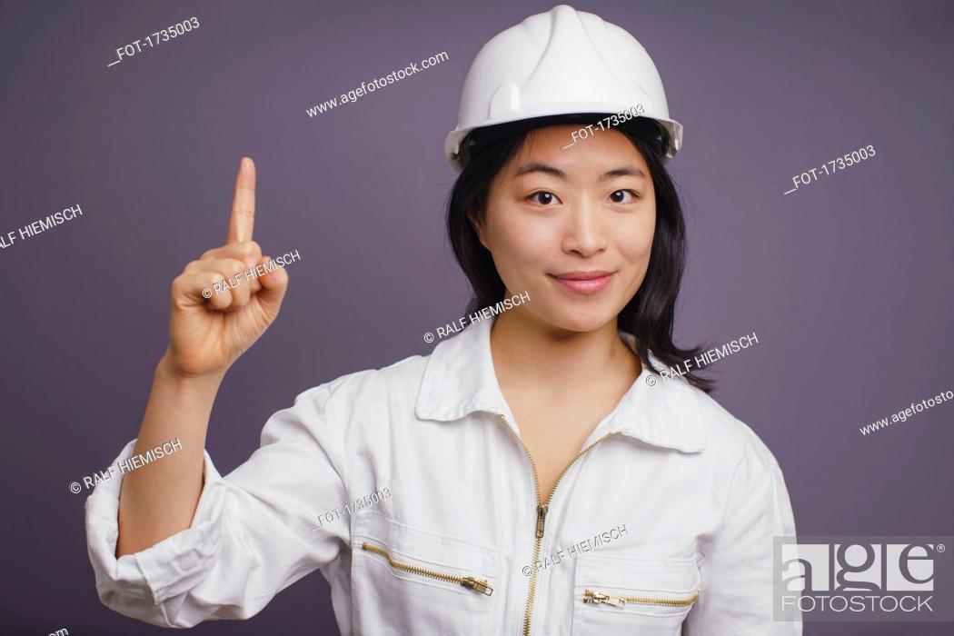 Stock Photo: Portrait of confident young female construction worker wearing hardhat pointing up.