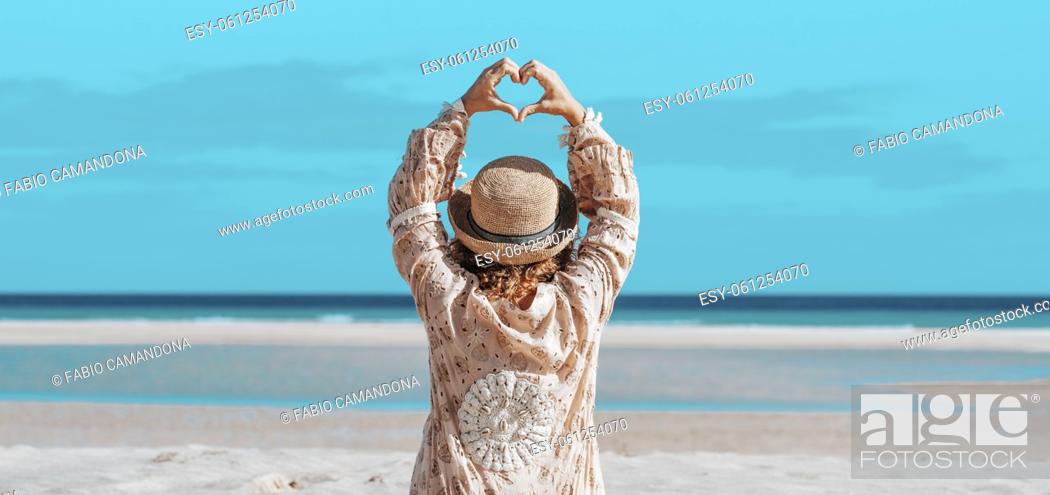 Photo de stock: Female tourist at the beach turning body and looking at the camera smiling happy. Cheerful young adult woman enjoy summer holiday vacation walking on the sand.