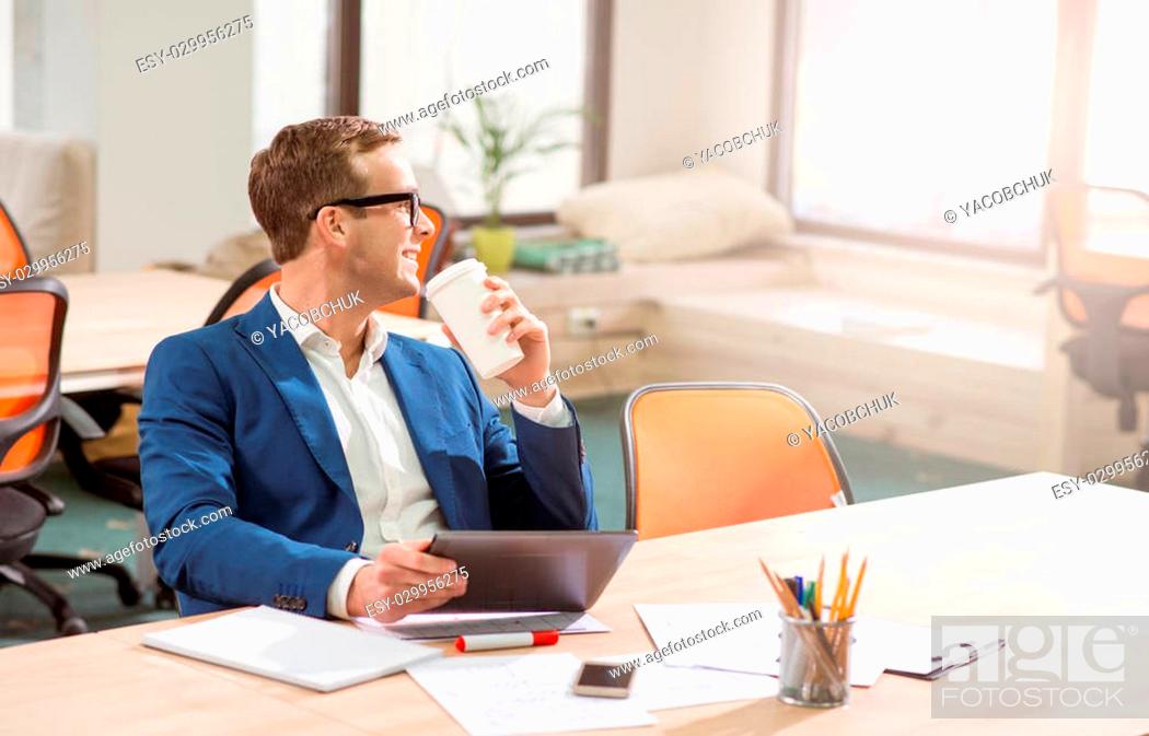 Stock Photo: Get some rest. Cheerful delighted handsome smiling man drinking coffee and holding tablet while sitting at the table.