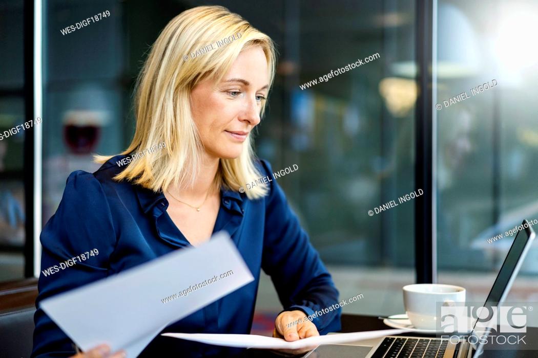 Imagen: Smiling businesswoman with documents looking at laptop.