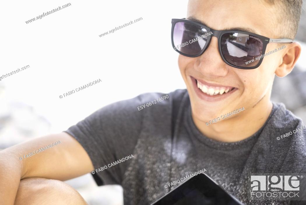 Stock Photo: Cheerful handsome teenage boy smiling in modern sunglasses with digital tablet. Happy male teenager having fun spending leisure time outdoors on a bright sunny.