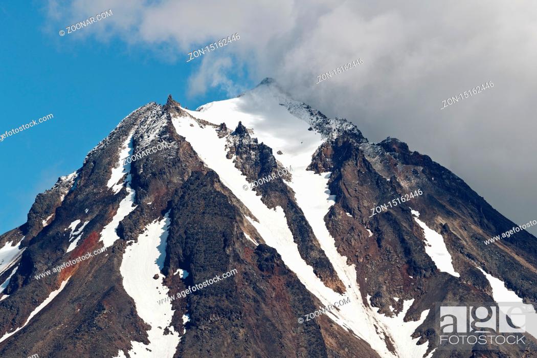 Photo de stock: Mountainous landscape of Kamchatka Peninsula: view of top of rocky cone of Vilyuchinsky Volcano, mountain peak and steep slope of volcano with snowfield.
