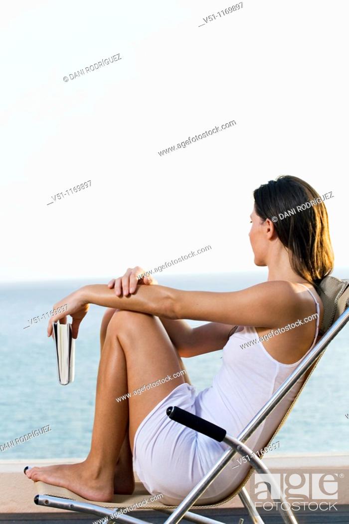 Stock Photo: Side view of a woman looking at the ocean from a terrace with a book.