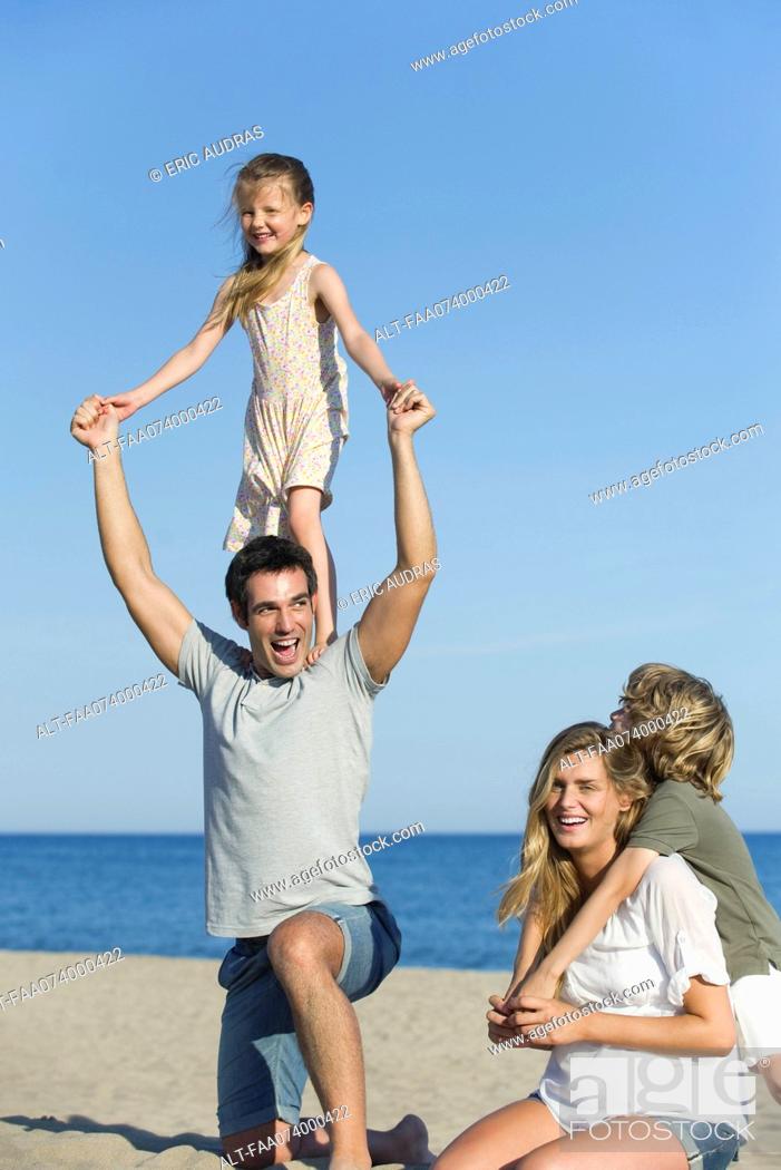 Photo de stock: Family playing together at the beach, girl standing on her father's shoulders.