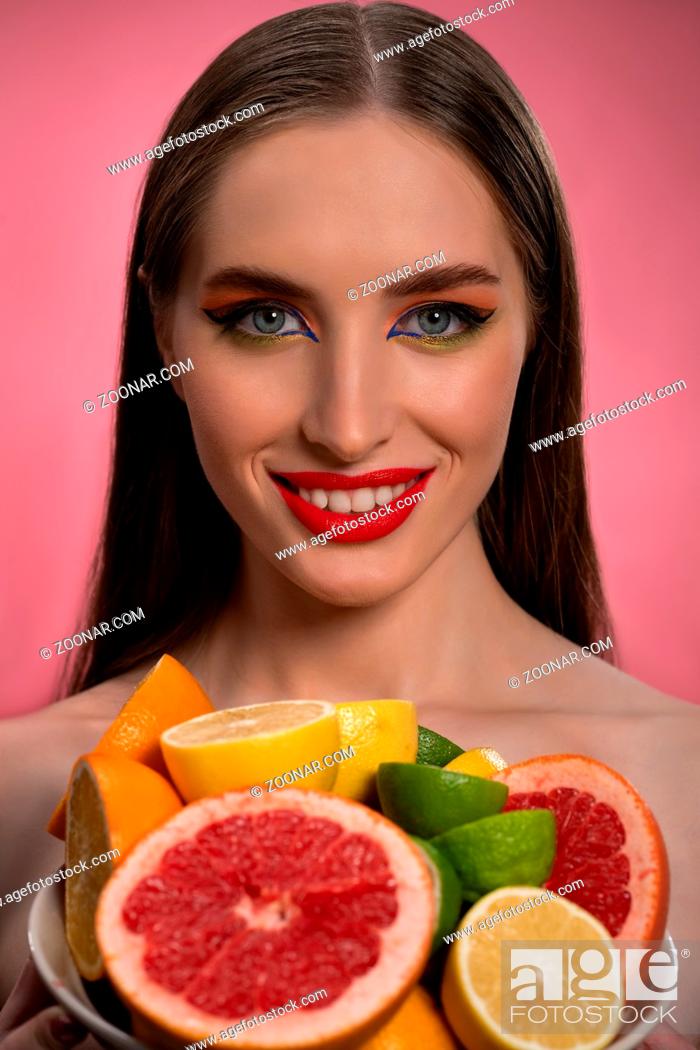Stock Photo: Beauty fashion model girl with beautiful make up, red lips, long healthy hair and bawl of colorful fresh cut citrus fruits in her hands.