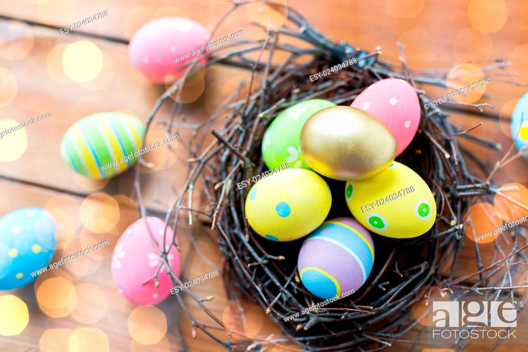 Stock Photo: easter, holidays, tradition and object concept - close up of colored easter eggs in nest on wooden surface over lights.