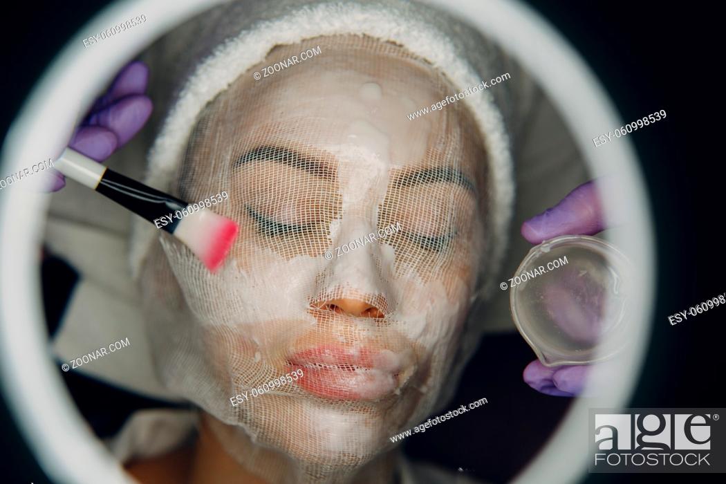 Stock Photo: Paraffin Face Mask gauze bandage Therapy Young Woman Receiving Facial Skin Care Treatment. Beautician Pouring Wax Applying.