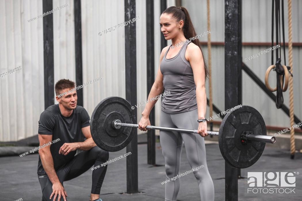 Stock Photo: Male instructor looking at young woman crossfit training at gym.
