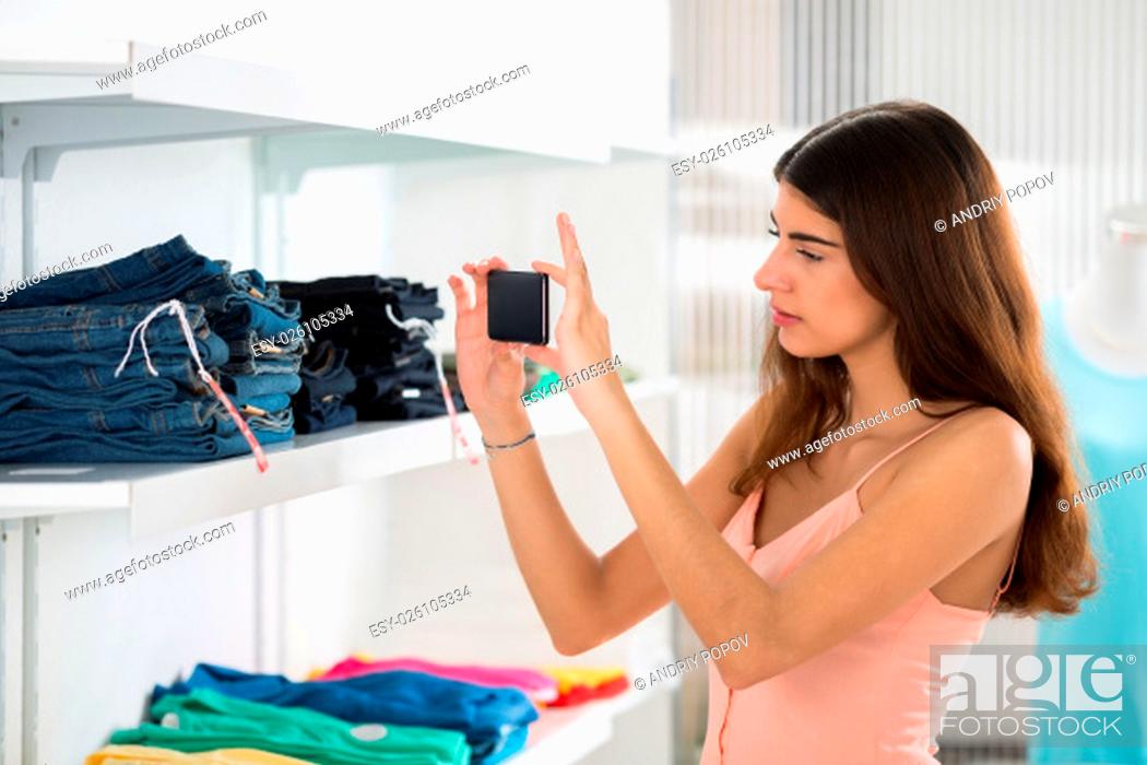 Stock Photo: Woman photographing jeans through smartphone in retail store.