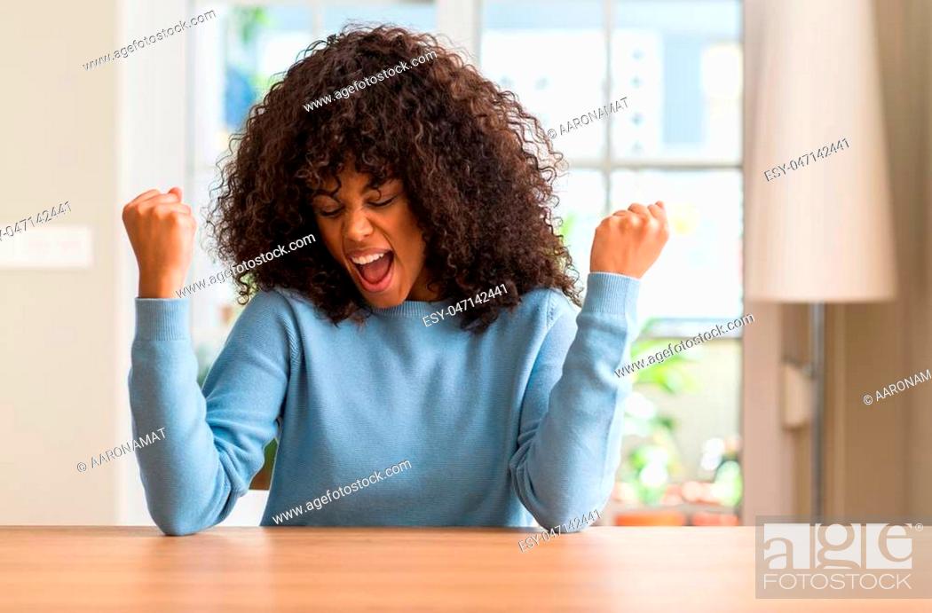 Stock Photo: African american woman at home very happy and excited doing winner gesture with arms raised, smiling and screaming for success. Celebration concept.