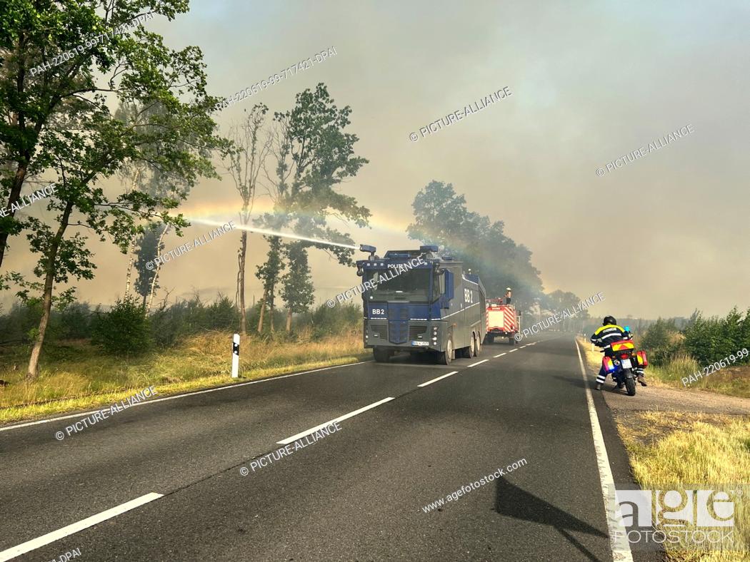 Stock Photo: 19 June 2022, Brandenburg, Treuenbrietzen: A police water cannon is in action in a forest fire. The area affected by the forest fire in Treuenbrietzen near.